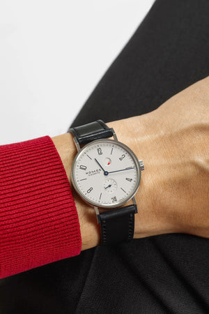 Watch on a wrist with a red sleeve against a neutral background