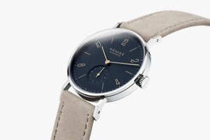 Nomos watch with a blue dial and beige strap on a white background