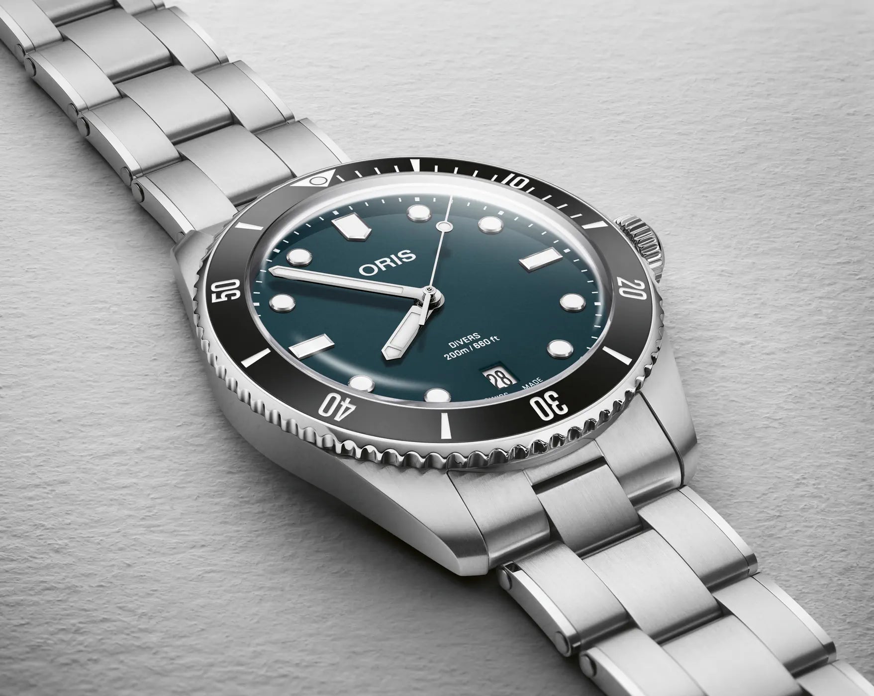 Silver Oris watch with a blue green face on a gray background