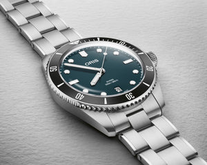 Silver Oris watch with a blue green face on a gray background