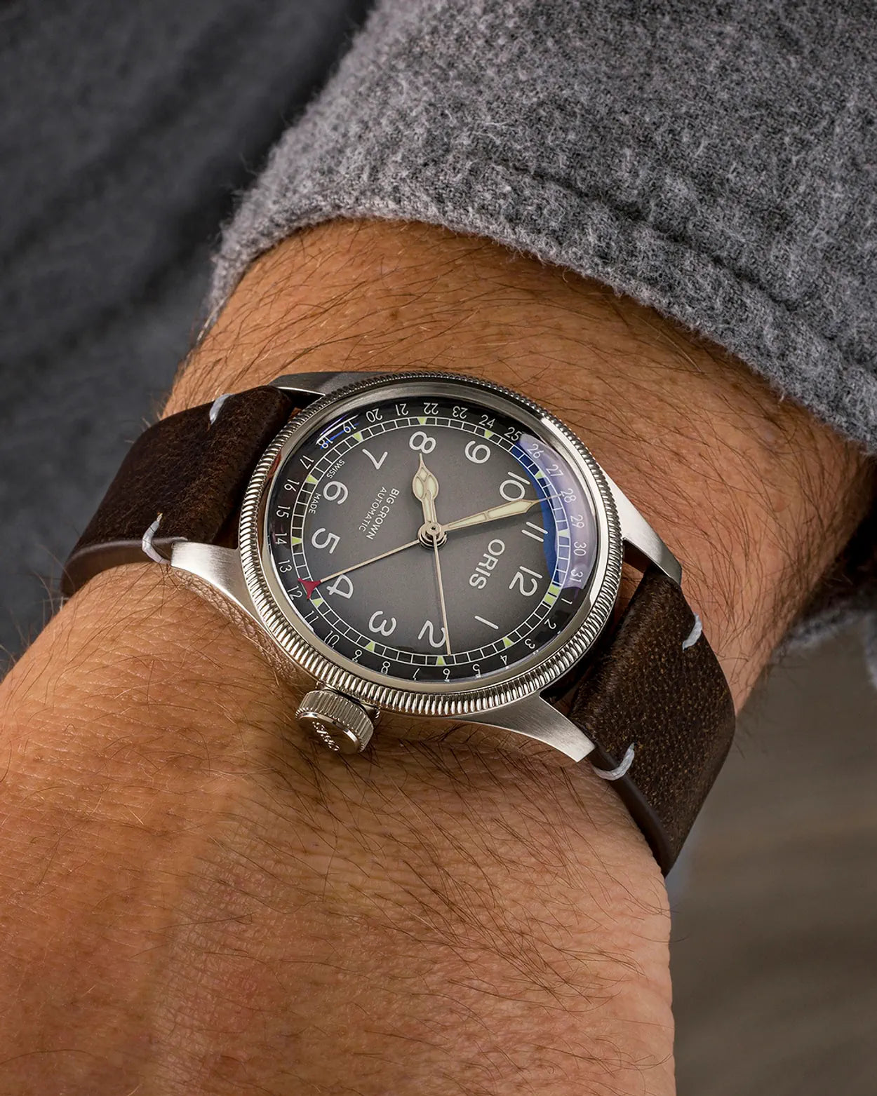 Vintage-style wristwatch with brown leather strap on a person's wrist against a blurred background