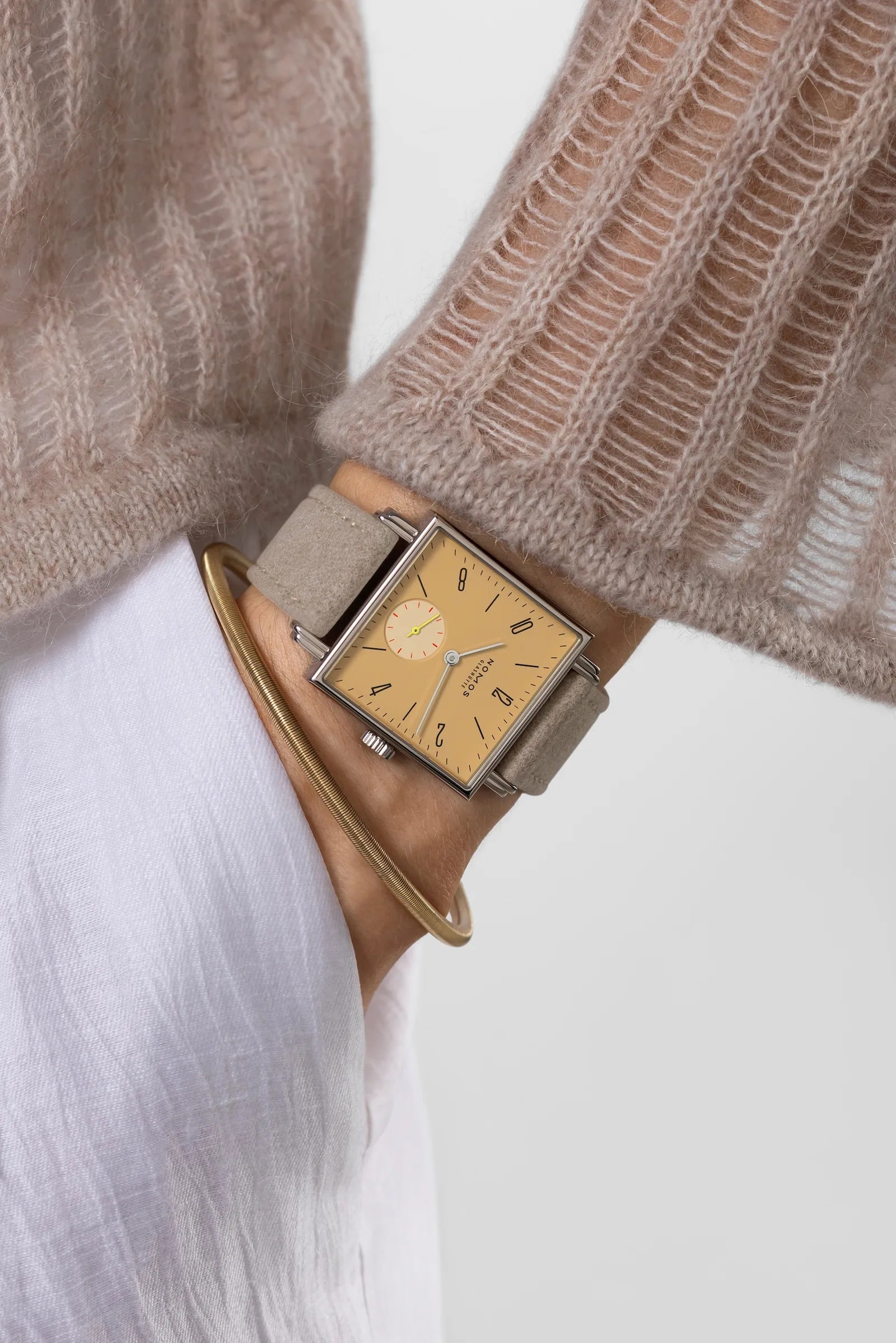 Person wearing a watch with a beige strap and beige dial on a white background