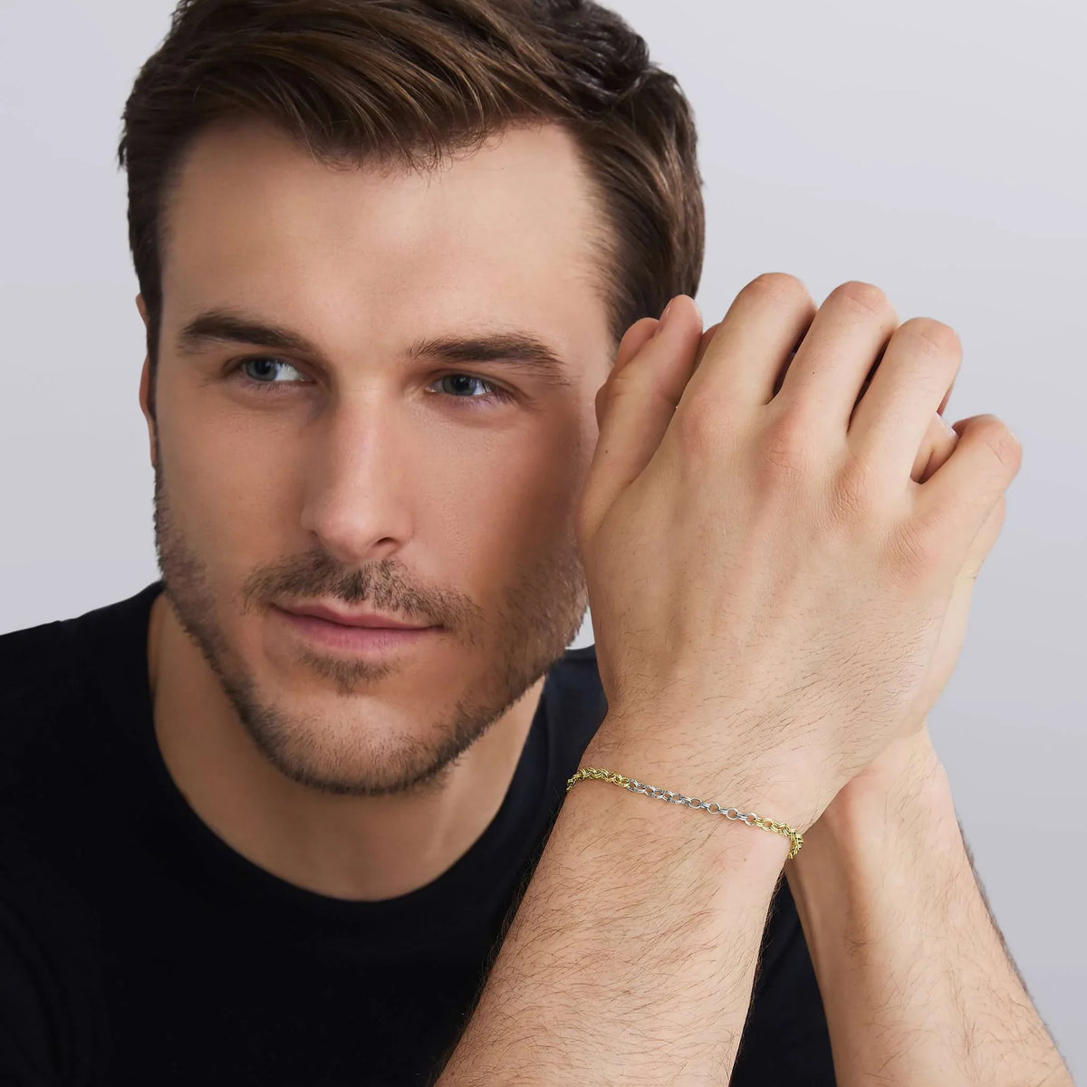 a man wearing a black shirt holding his hands wearing a two tone bracelet on a white background