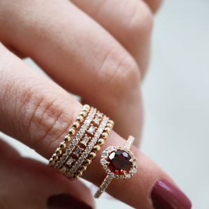 Close-up of round and baguette diamond ring on finger showing red center stone haloed by diamonds and rose gold bands