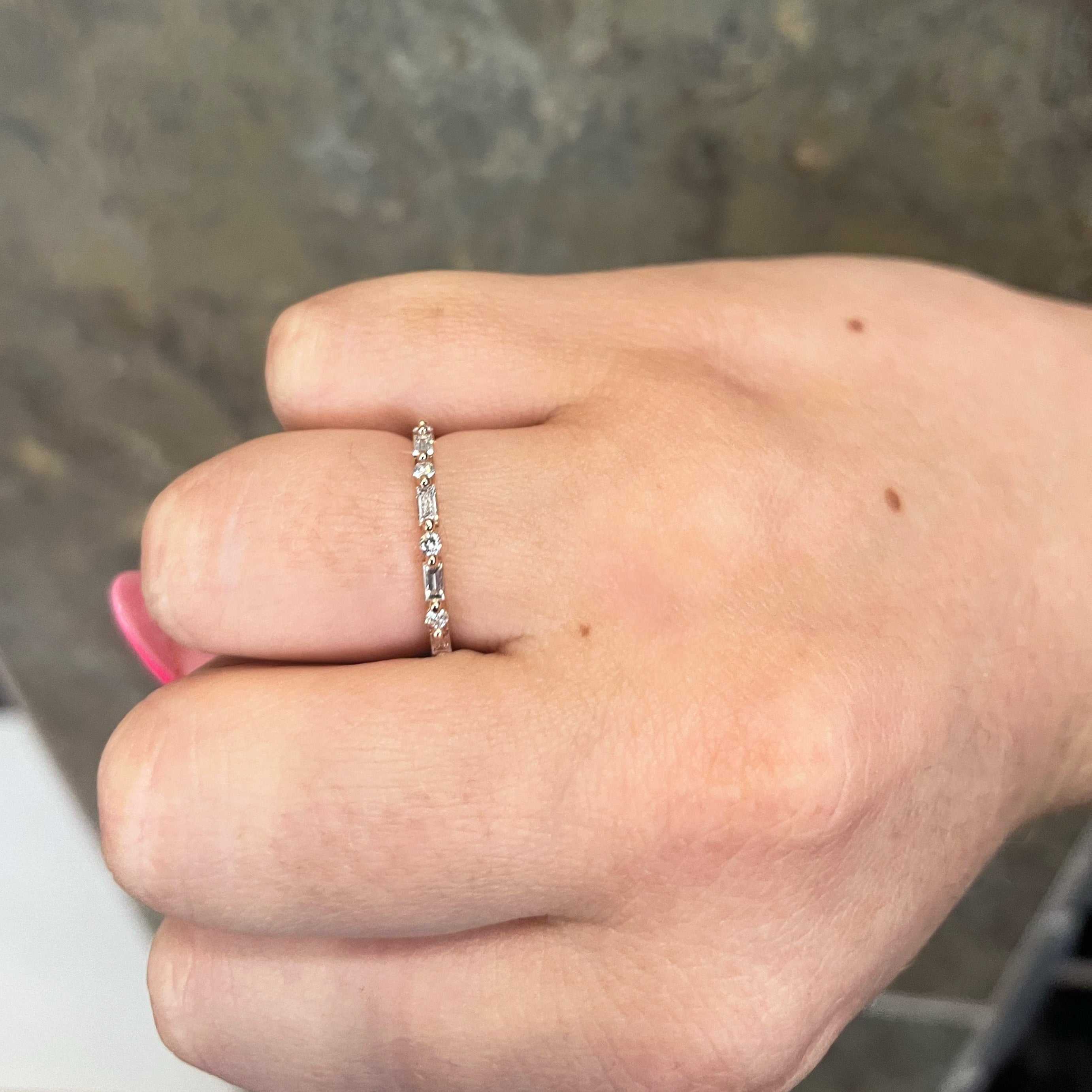 Thin band ring with alternating round and baguette diamonds worn on a finger