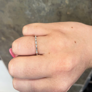 Thin band ring with alternating round and baguette diamonds worn on a finger