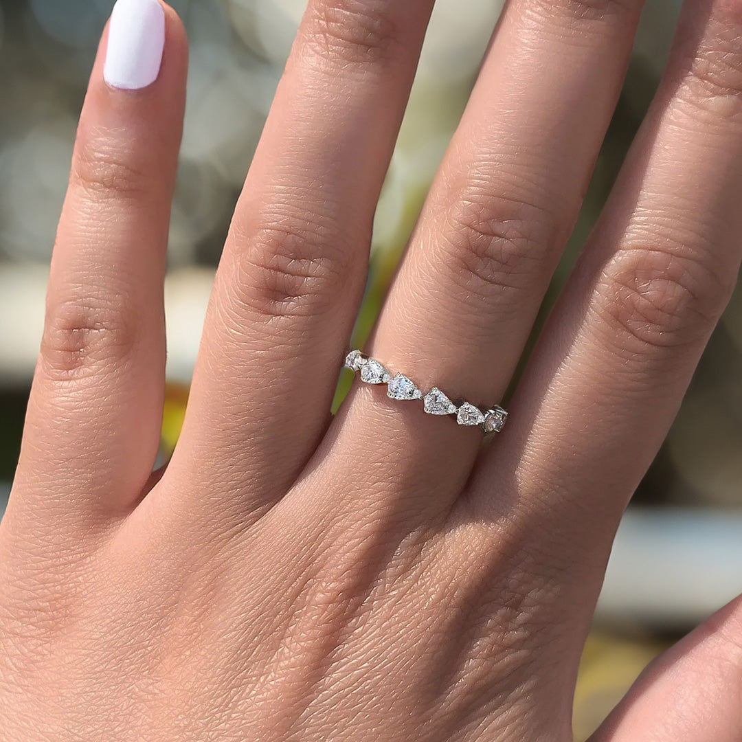 Hand with pale-pink manicure wearing a thin band of five pear-shaped diamonds on the ring finger.