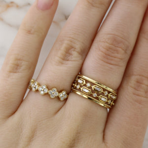 Two gold rings on adjacent fingers — delicate diamond floral band and wider engraved band with rectangular settings.