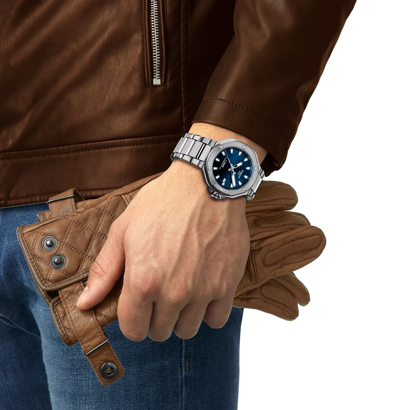 Person wearing brown leather jacket and jeans holding brown leather gloves wearing a Tissot watch with blue dial on a white background