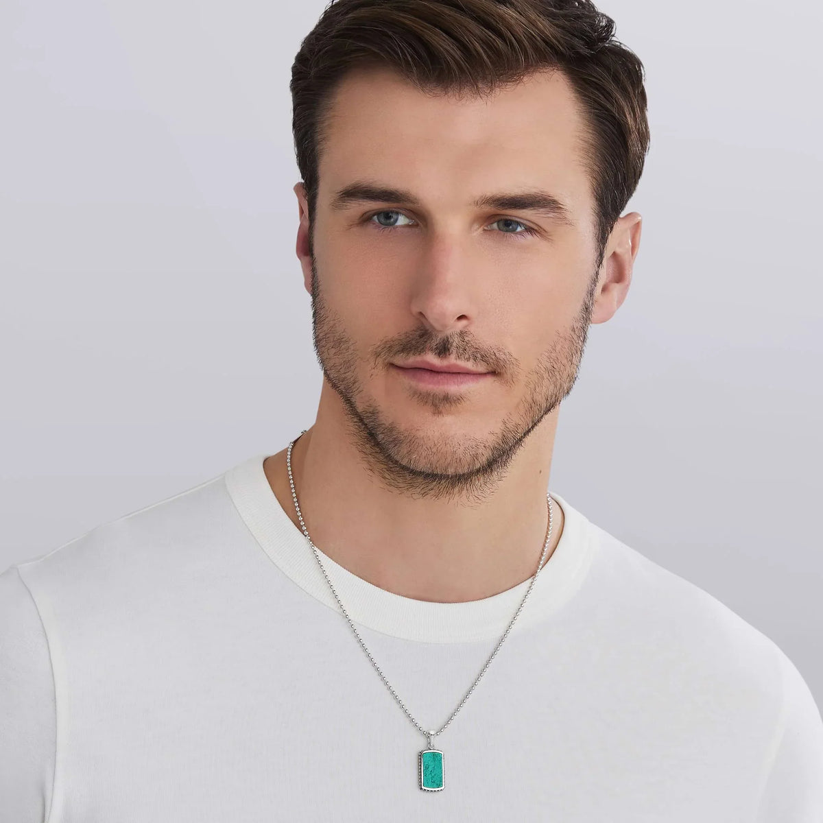 a man wearing a white tshirt and a Sterling Silver and Turquoise Tag Amulet with beading around the edges on a white background