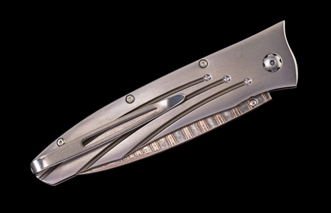 Closed William Henry Saturn III folding knife with titanium handle and decorative milled spine on black background.