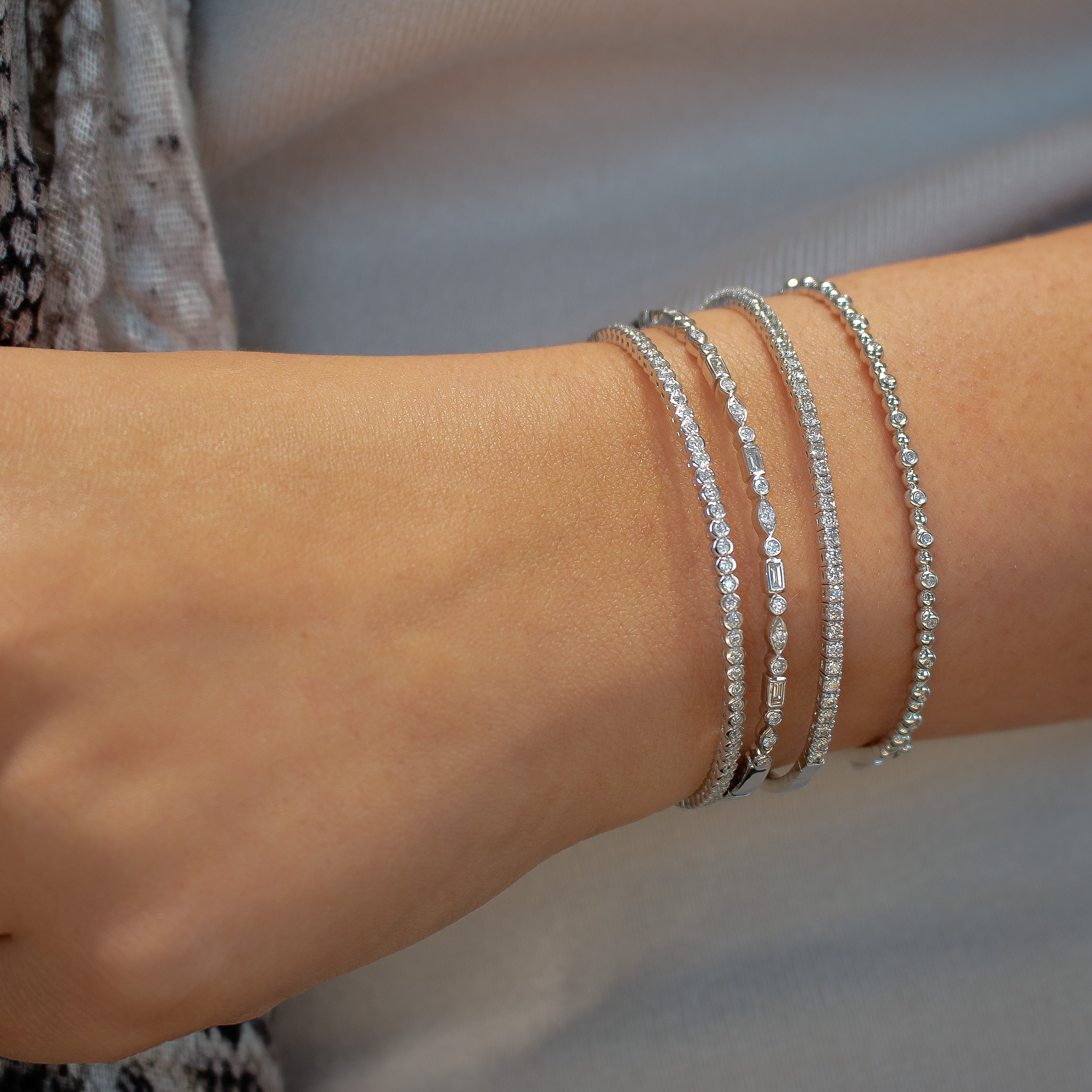Four delicate silver diamond bracelets layered on a woman's wrist, close-up.