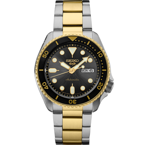 A Seiko automatic watch with a two-tone stainless steel and gold-tone link bracelet, featuring a black dial, black bezel, and gold-tone hour markers.