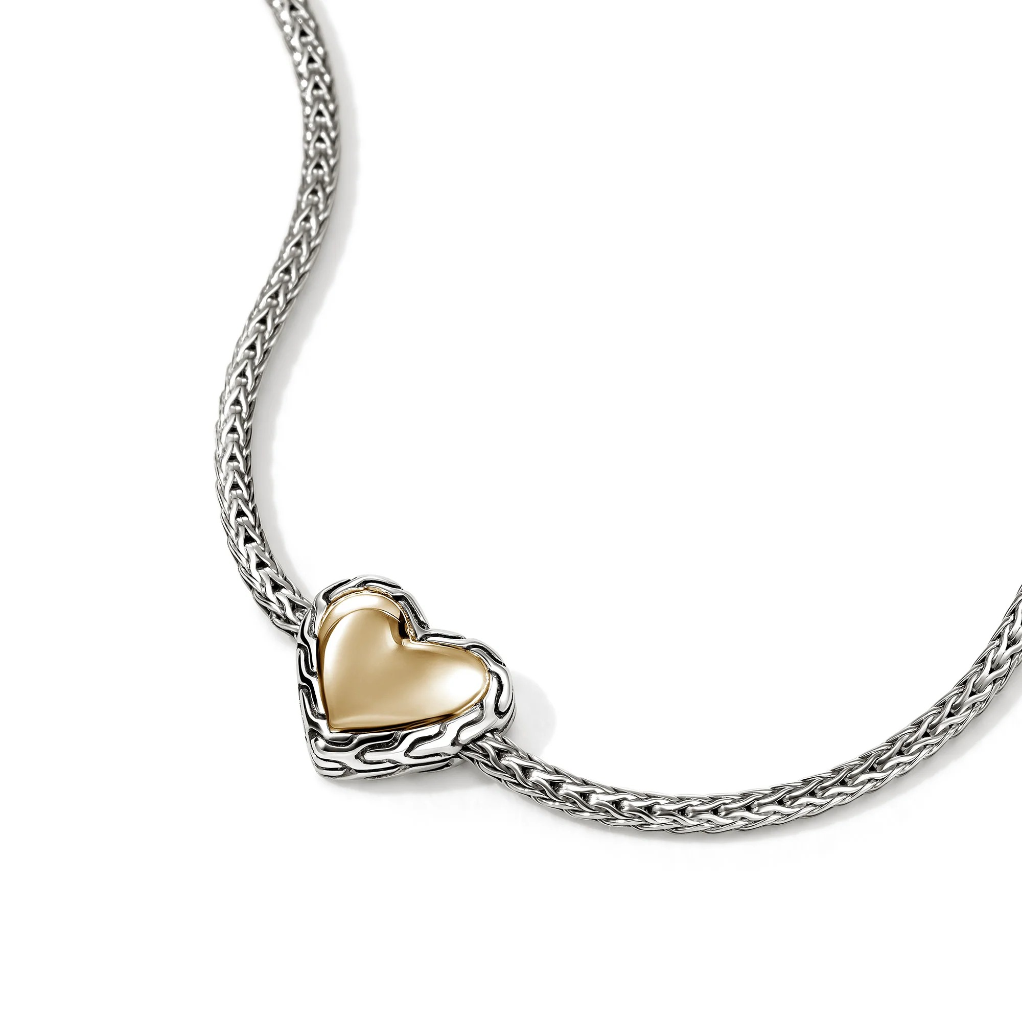 Close-up of Essential Heart Bracelet showing two-tone gold heart with carved sterling silver border on chain on white