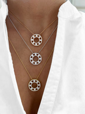 Three layered necklaces with circular ring pendants are shown worn on a model's neck. The necklaces have different metals: one silver-tone, one gold-tone, and one rose gold-tone, each adorned with small clear stones.