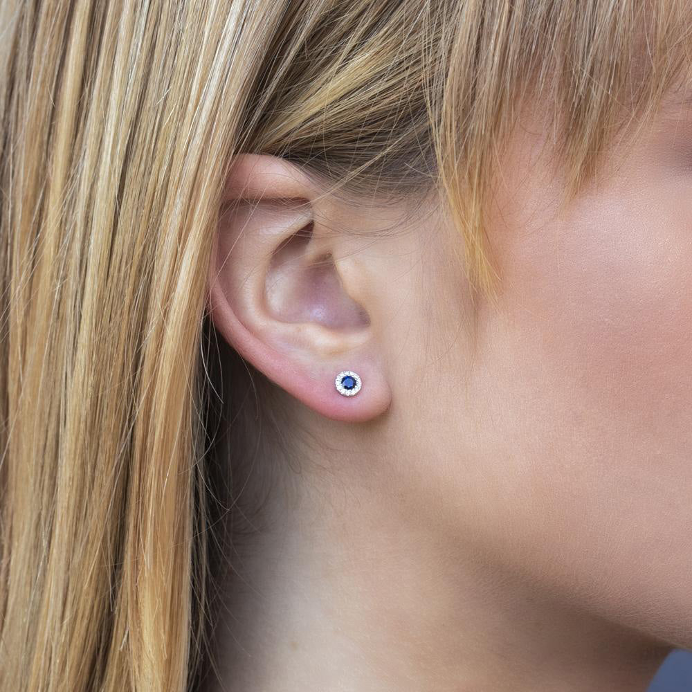 Close-up of a blonde woman's ear wearing a small sapphire center halo stud earring