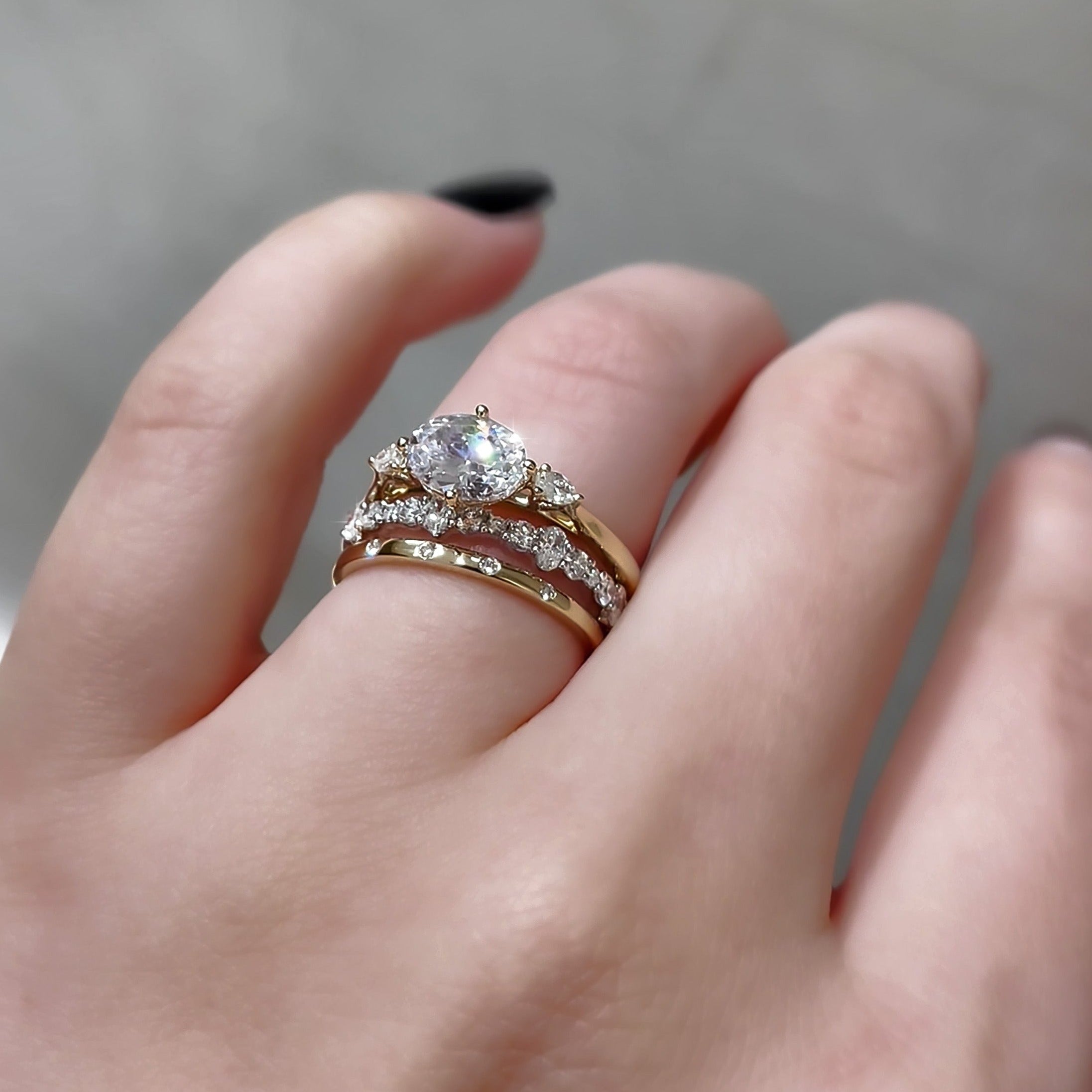 Close-up of .58ctw oval and round shared prong eternity band stacked with engagement band on finger, blurred background