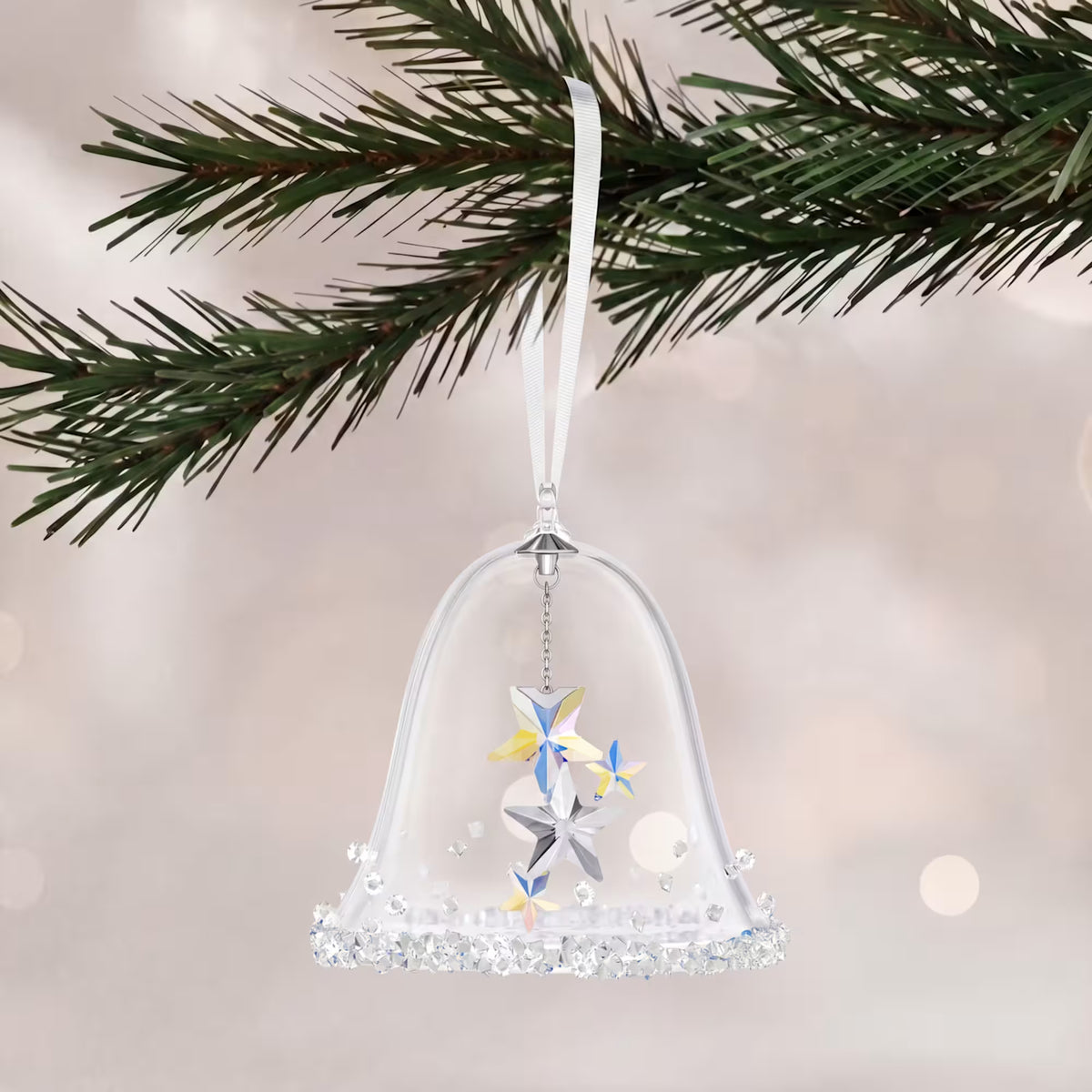 a glass and crystal bell hanging from a tree on a white shimmery background