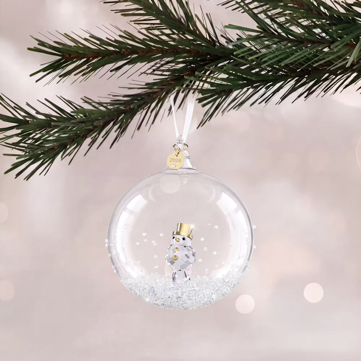 glass ball ornament with crystals and  with 2026 engraved on a gold tone plated tag with white ribbon hanging from a tree on a white shimmery background