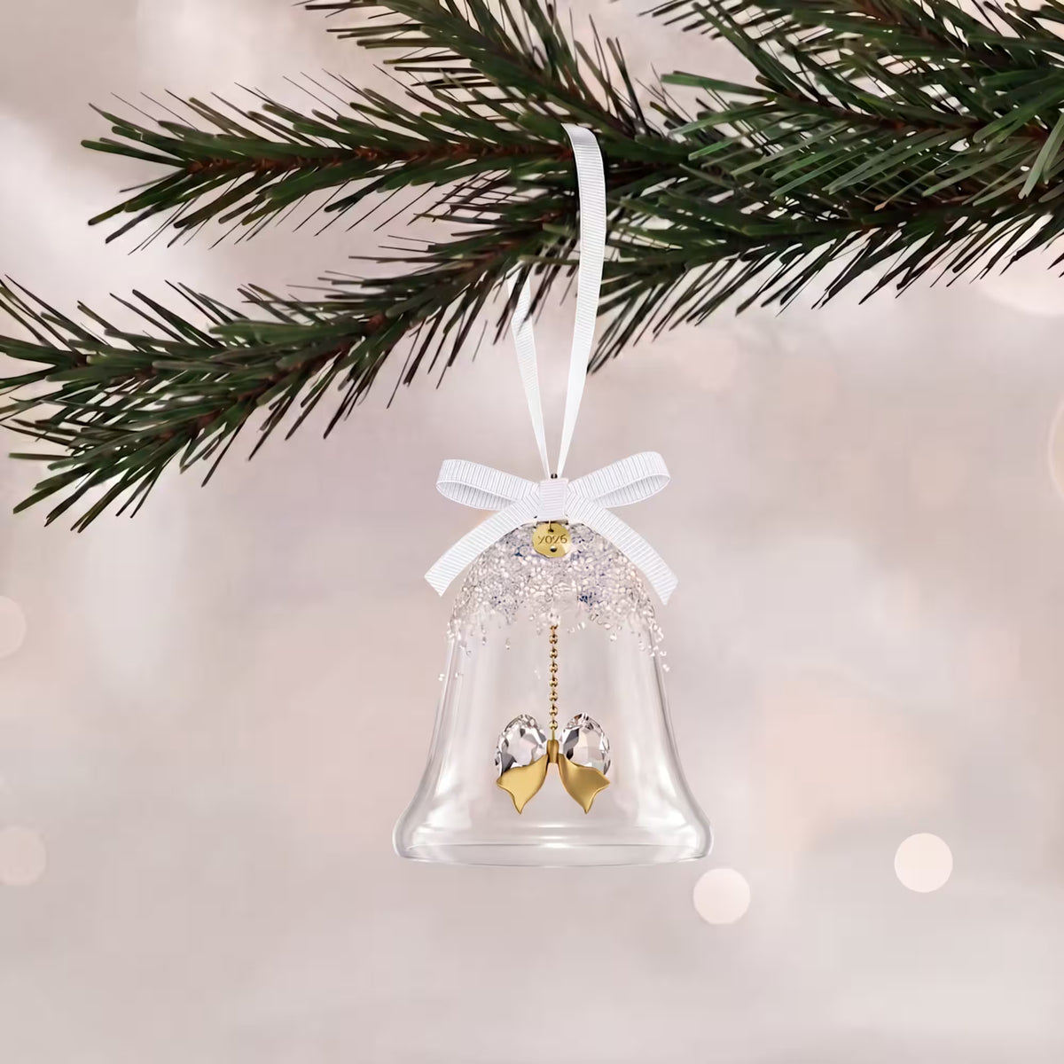 glass bell with crystals with gold tone finishes and plated tag with 2026 engraved with white ribbon hanging from a tree on a white shimmery background