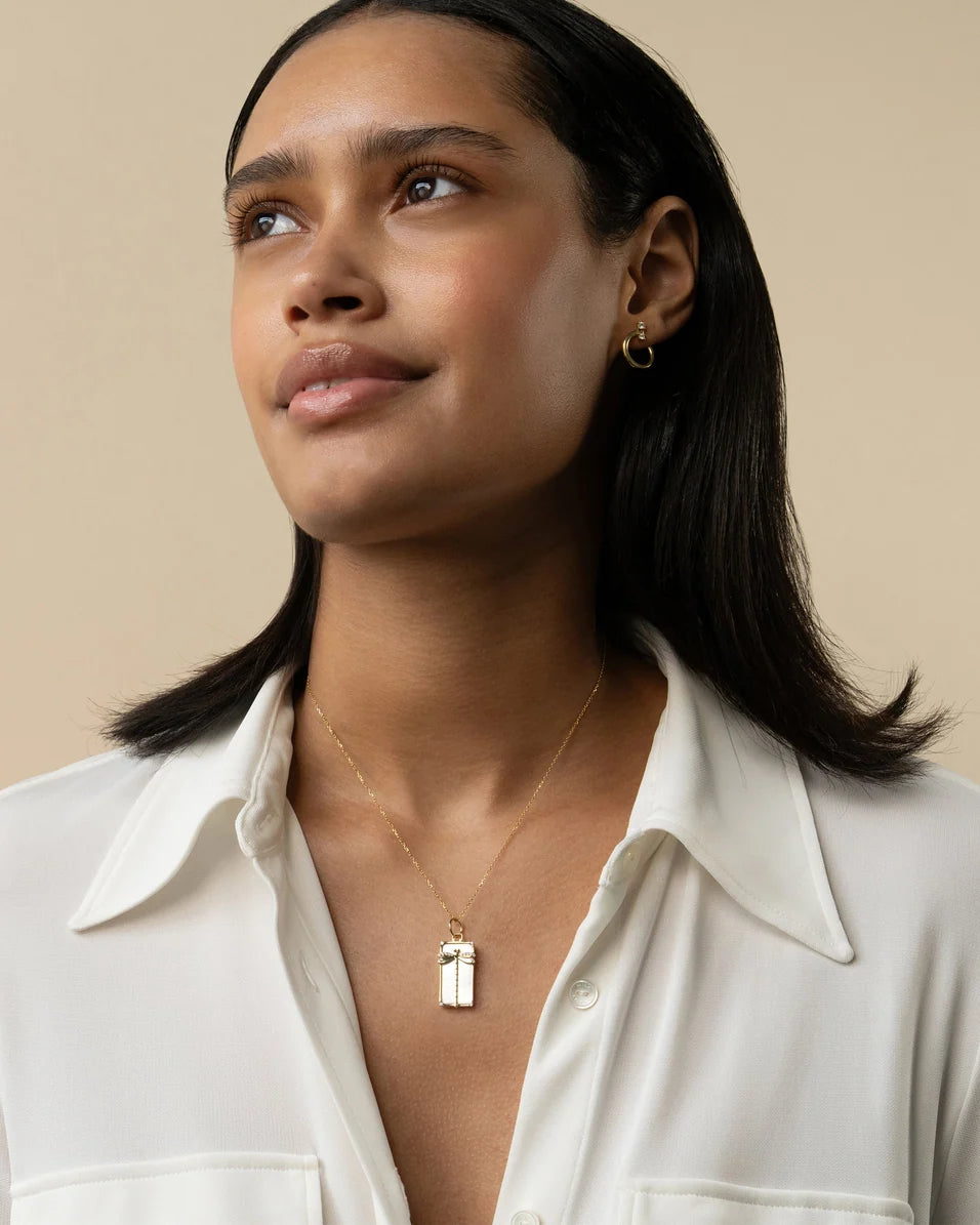 a woman wearing a white shirt with a yellow gold necklace on a beige background