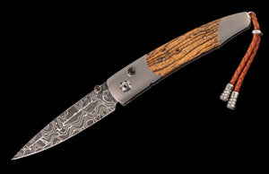 Angled view of William Henry Fresh knife showcasing Damascus blade, titanium frame and bocote wood inlay on black background