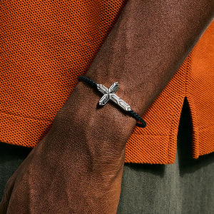 Silver cross bracelet on a wrist with an orange textured background