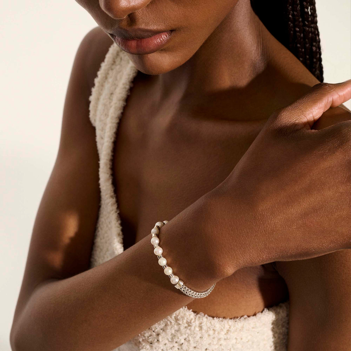 a lady wearing a white top with her hand on her shoulder with a pearl and silver bracelet on.