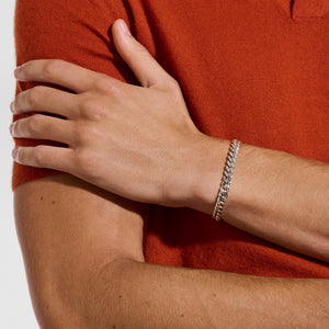 a man wearing a orange shirt hand on arm wearing a silver curb chain bracelet on a white background