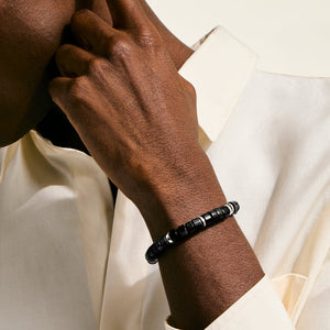 Hand wearing a black beaded bracelet on a light background