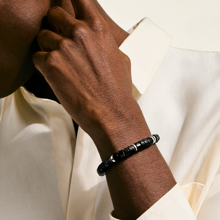 Hand wearing a black beaded bracelet on a light background
