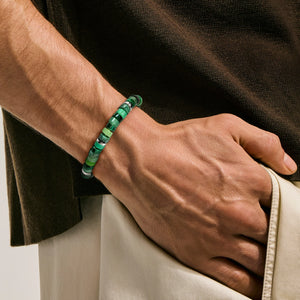 A close-up of a person's wrist wearing a green beaded bracelet, with their hand resting in a light-colored pocket.