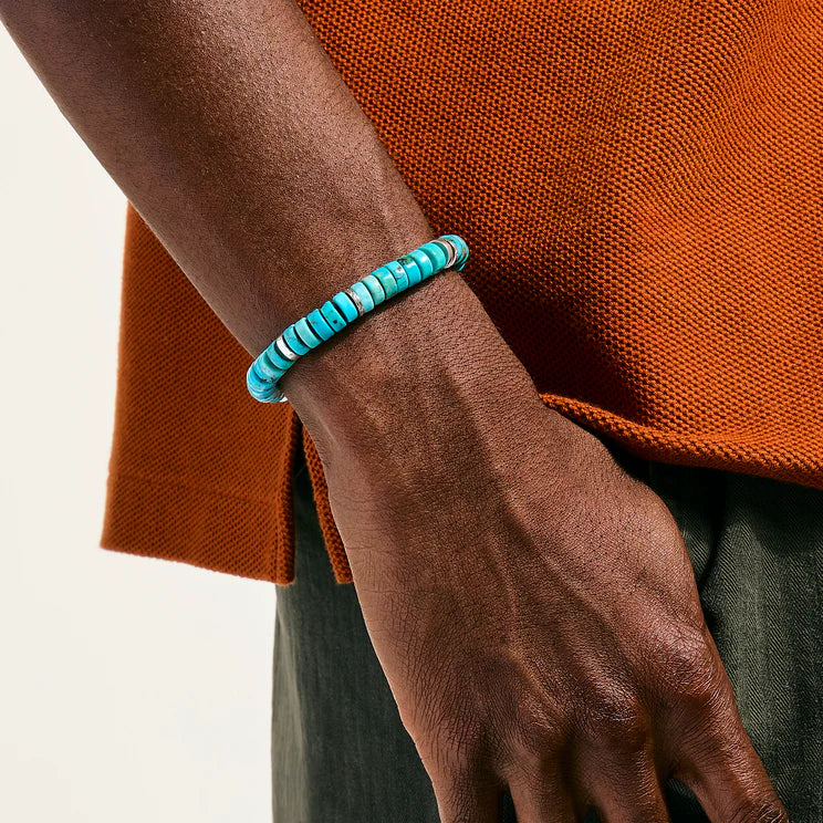 Turquoise beaded bracelet on a wrist with an orange garment in the background