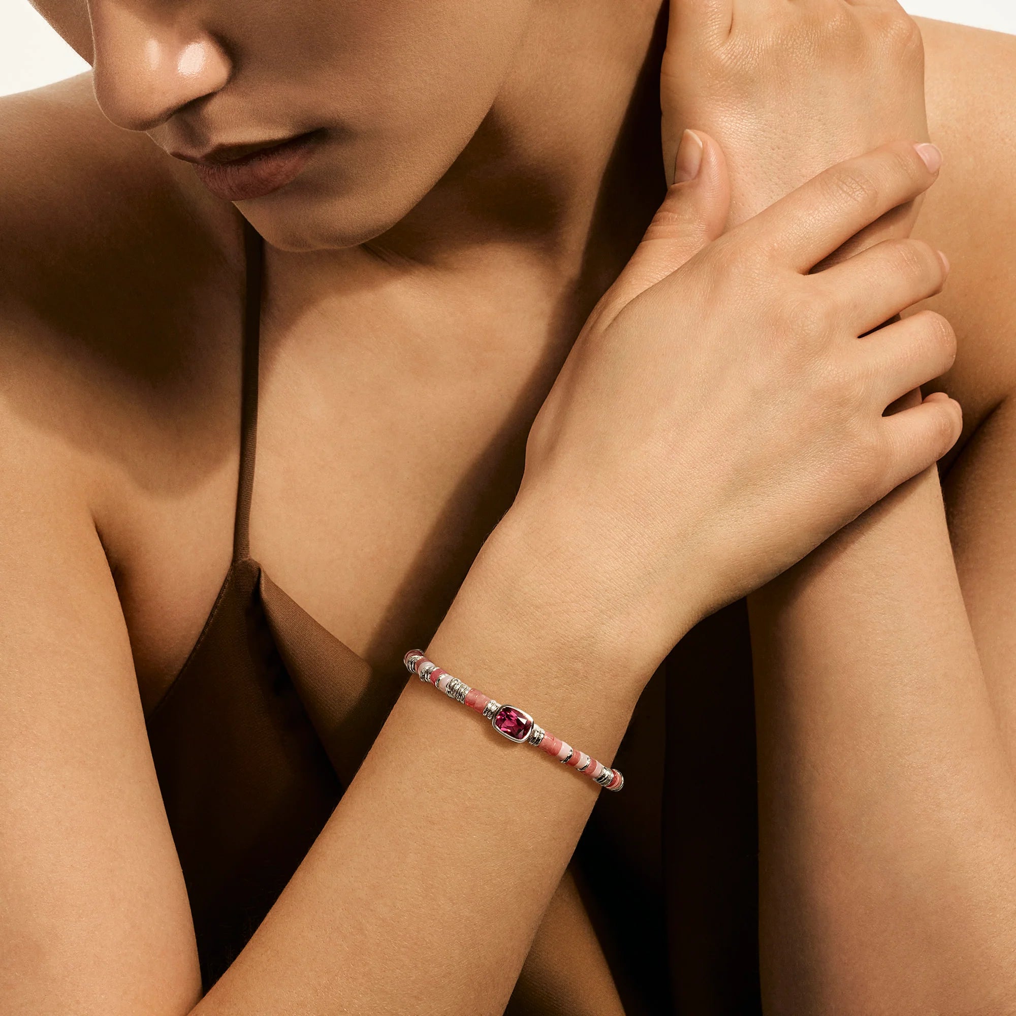 Close-up of a person wearing a pink colored stones bracelet on a neutral background