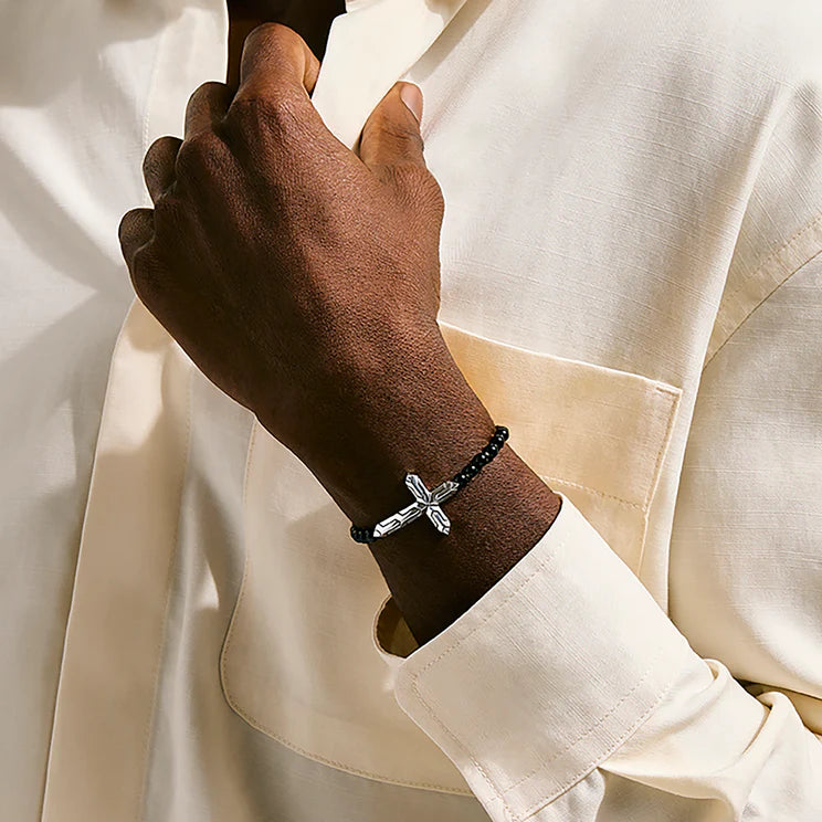 Hand wearing a bracelet with a cross charm on a white background