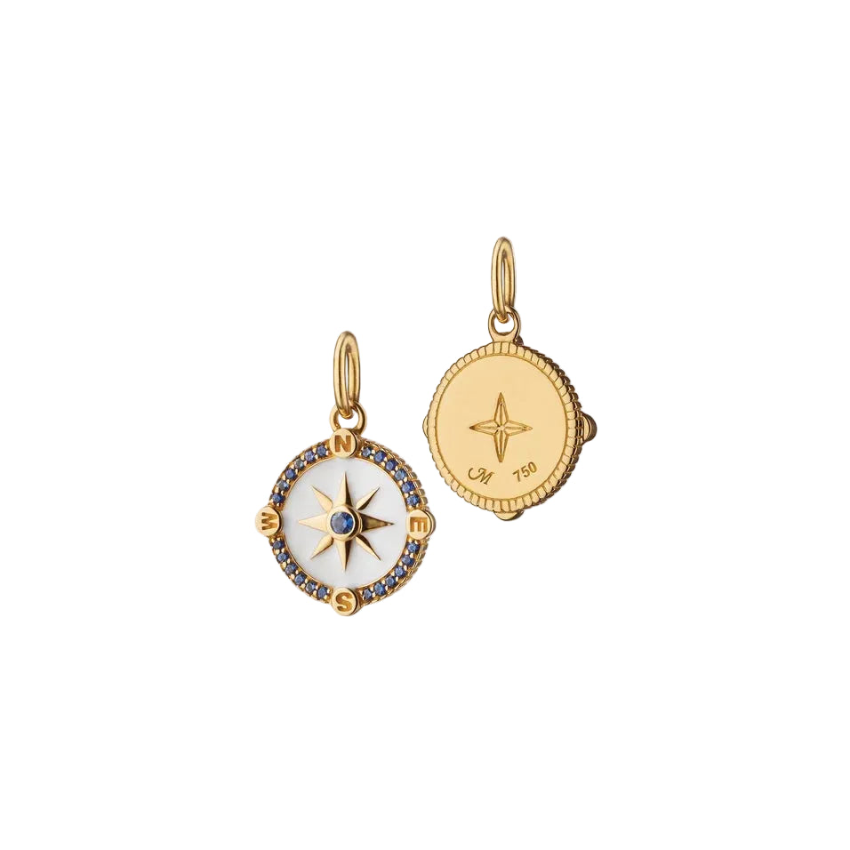 gold mini compass charm with white enamel and blue sapphires on a white background