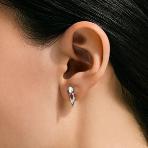 A close-up of a person's ear wearing a small silver twisted leaf-shaped stud earring.