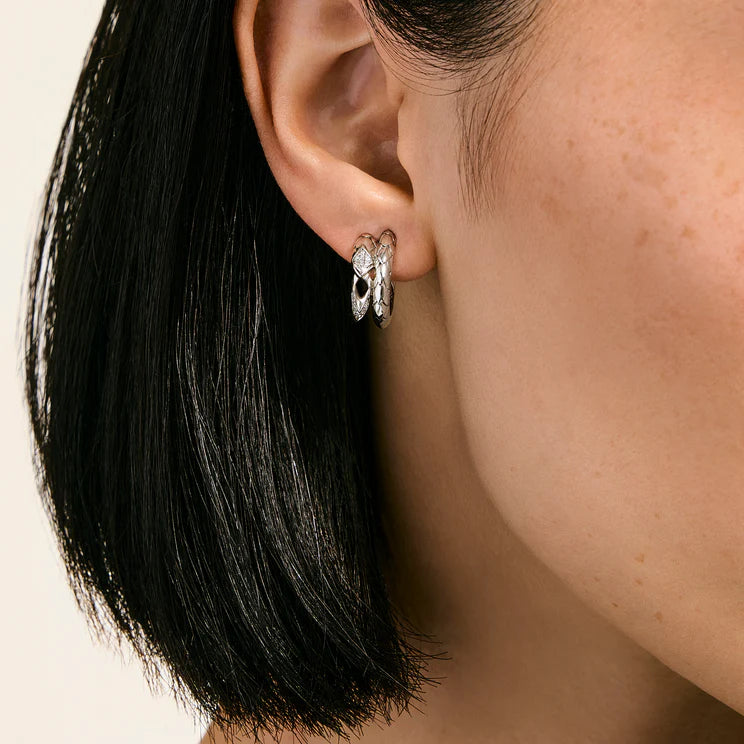 A close-up of a model's ear wearing a silver hoop earring with a textured, organic leaf-like design.