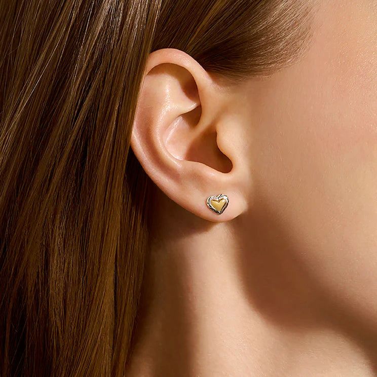 Close-up of an ear wearing a gold heart-shaped earring with hair partially obscuring the view.