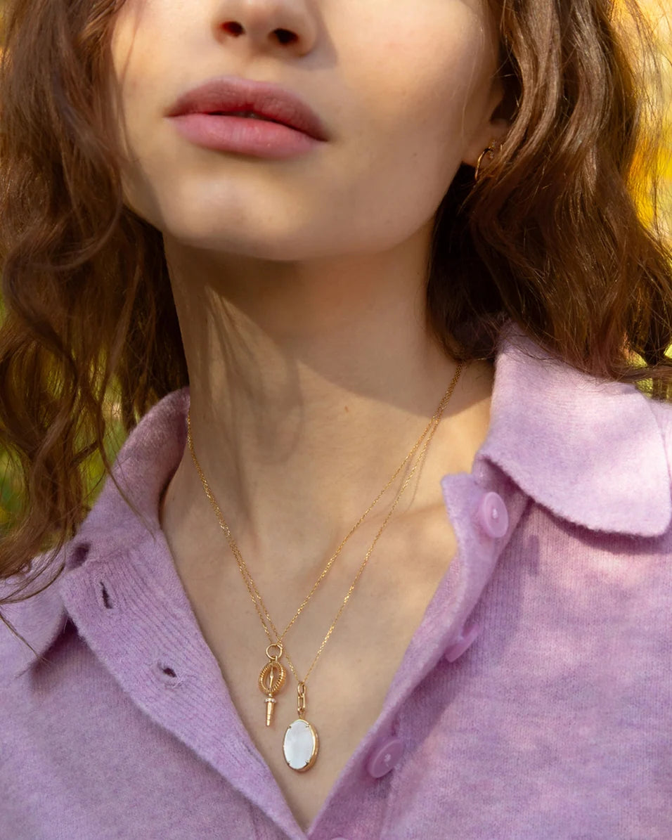 up close of a woman wearing a purple sweater and a gold compass necklace