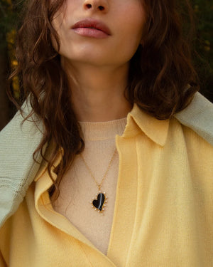 a woman wearing yellow sweaters and a black heart gold necklace