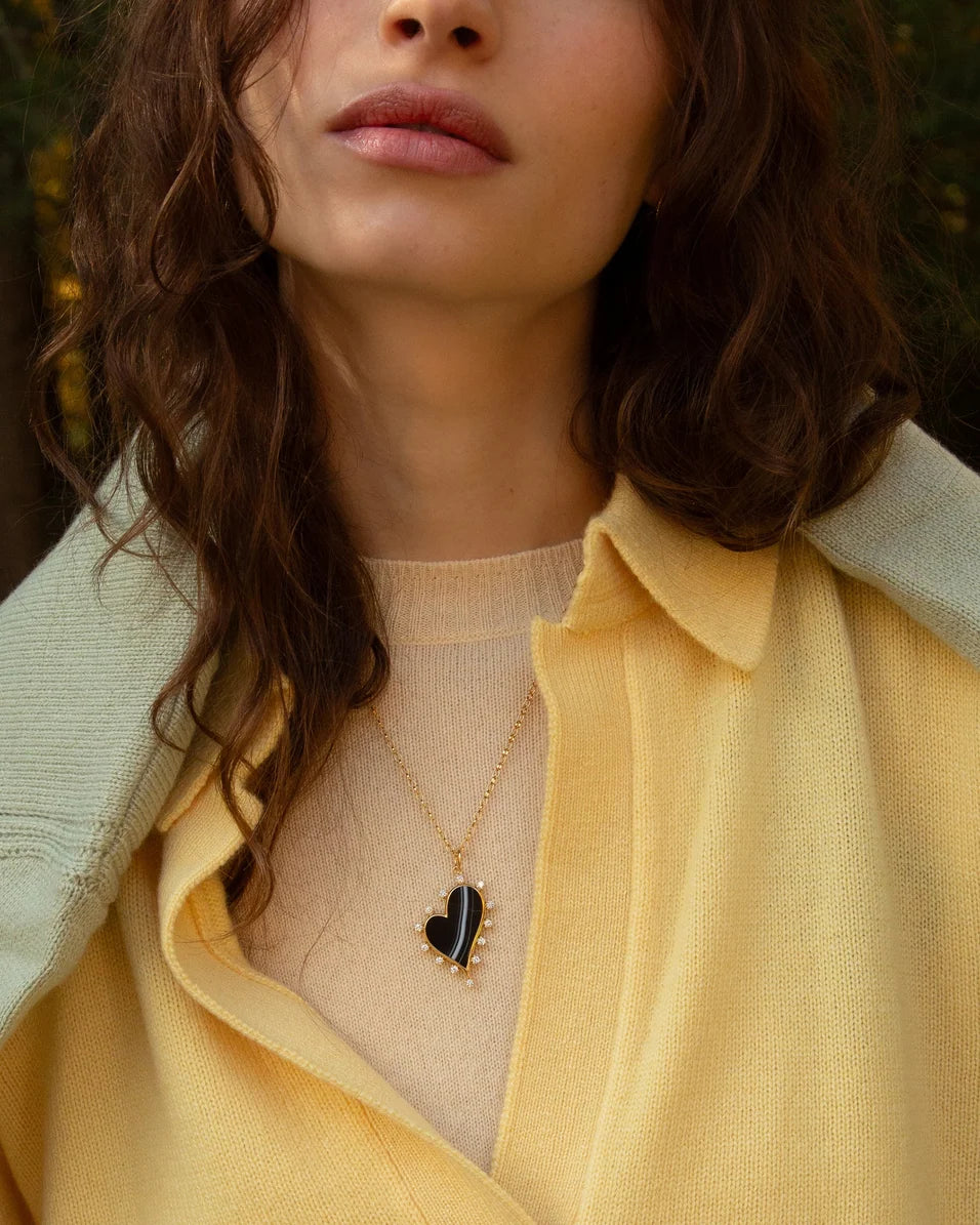 a woman wearing yellow sweaters and a black heart gold necklace