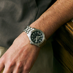 Close-up of a wrist wearing a silver watch with a black face.