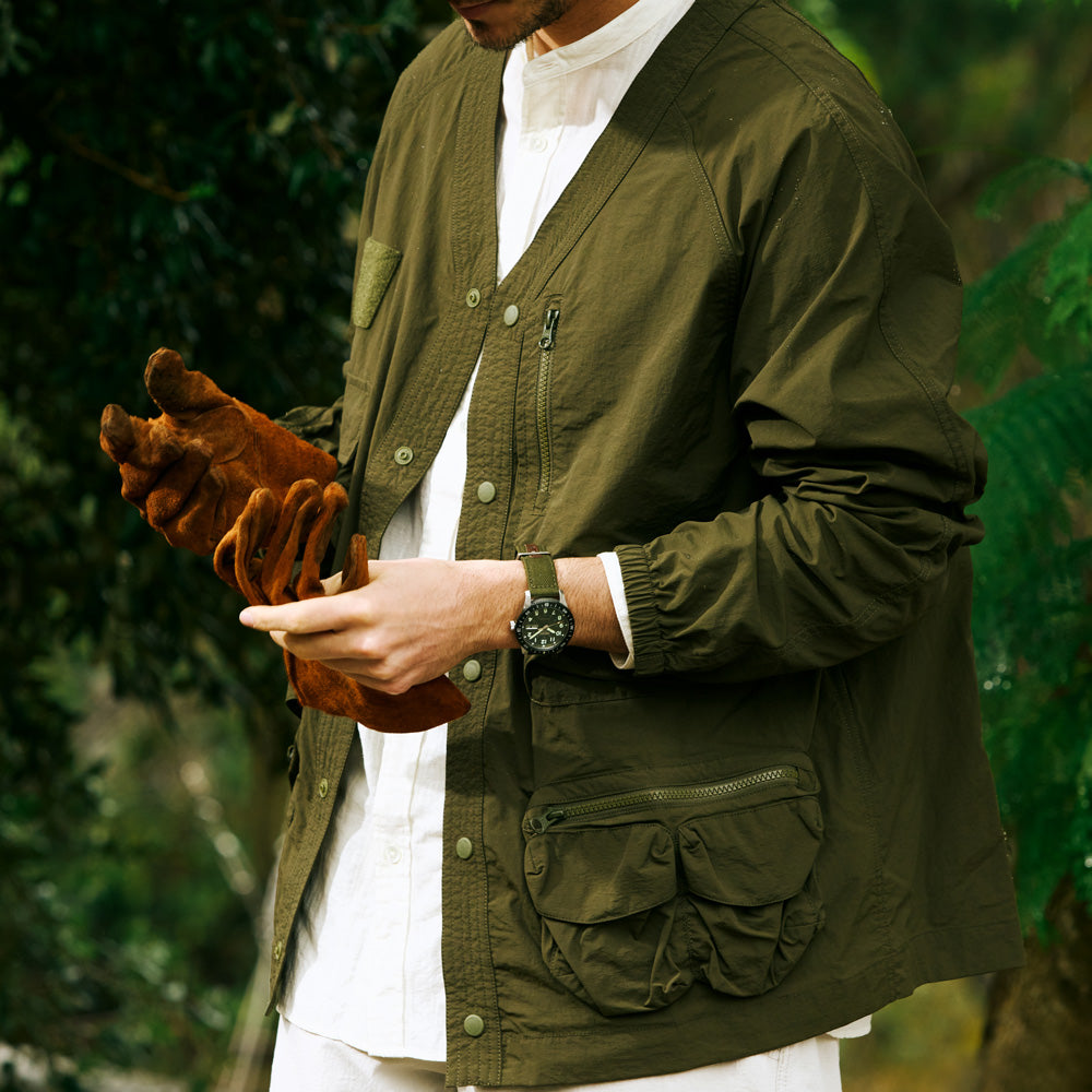 Person wearing a green jacket holding brown gloves with a blurred green background