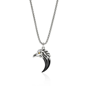 A silver-toned metal pendant necklace featuring a stylized raven or eagle head with a glossy black enamel fill and a small yellow eye, suspended from a silver chain on a white background.