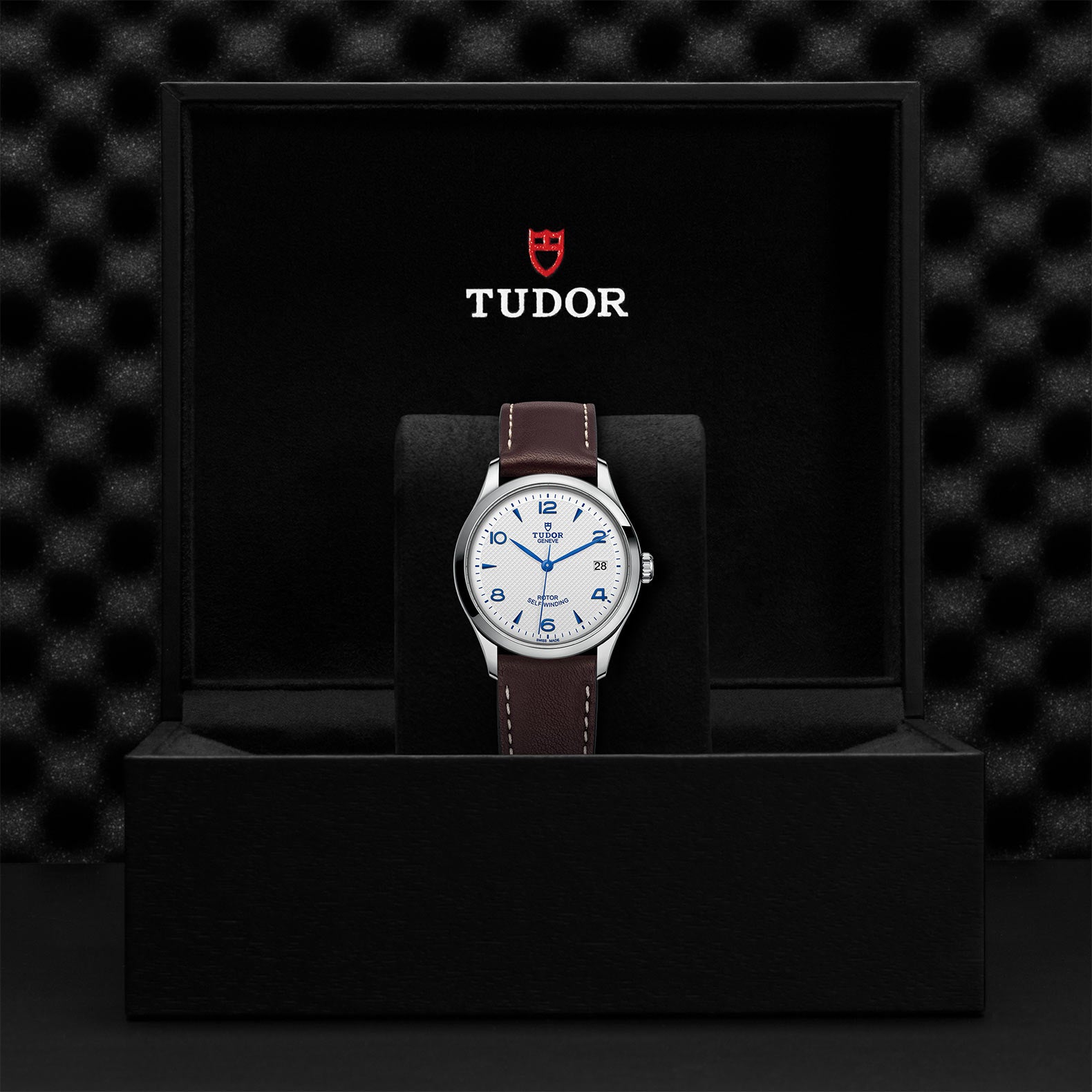 Front view of Tudor 1926 36mm steel watch with opaline dial, blue hands and brown leather strap in black Tudor box