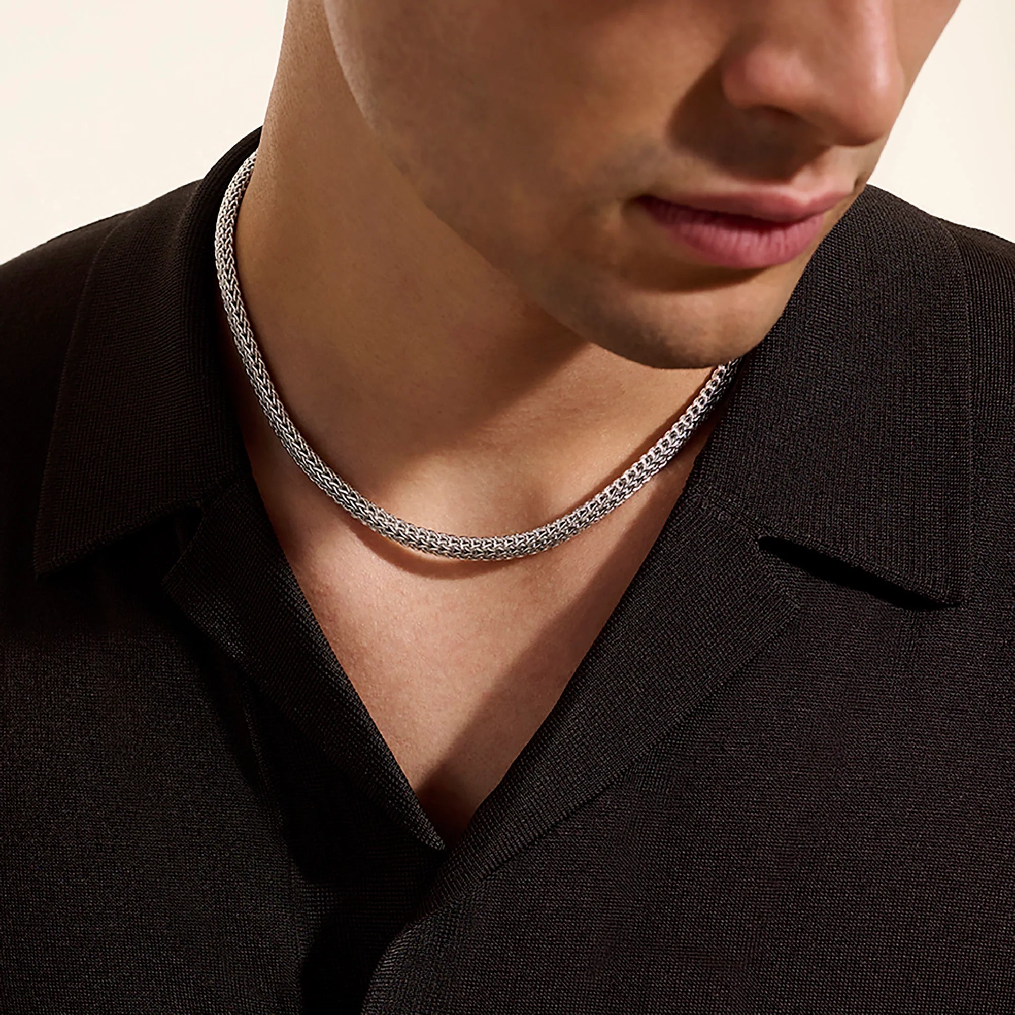 Person wearing a silver chain necklace against a neutral background