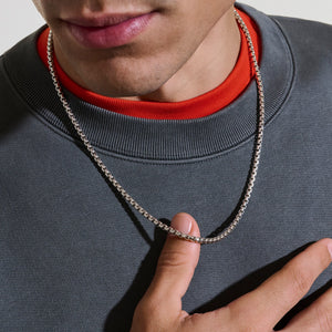 a man wearing a grey shirt with a silver necklace on a white background