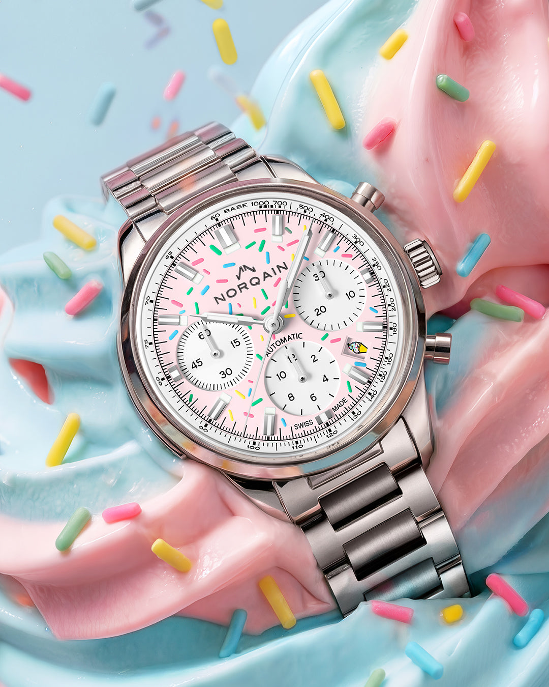Angled close-up of Norqain Freedom Chrono Sprinkles watch with pink sprinkle dial, chronograph subdials and steel bracelet