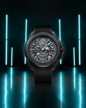 Black wristwatch with detailed face on a reflective surface with blue lights in the background